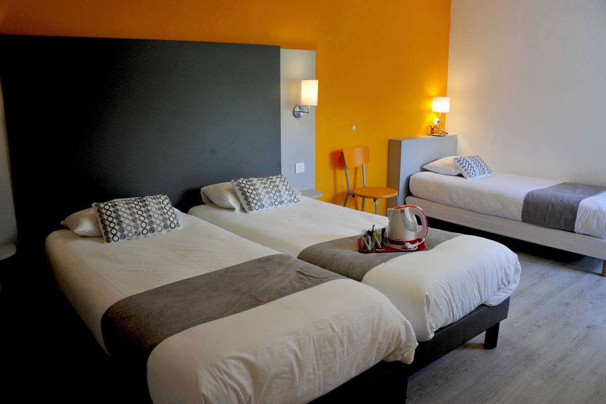 A hotel room with two beds, a chair, and a lamp.