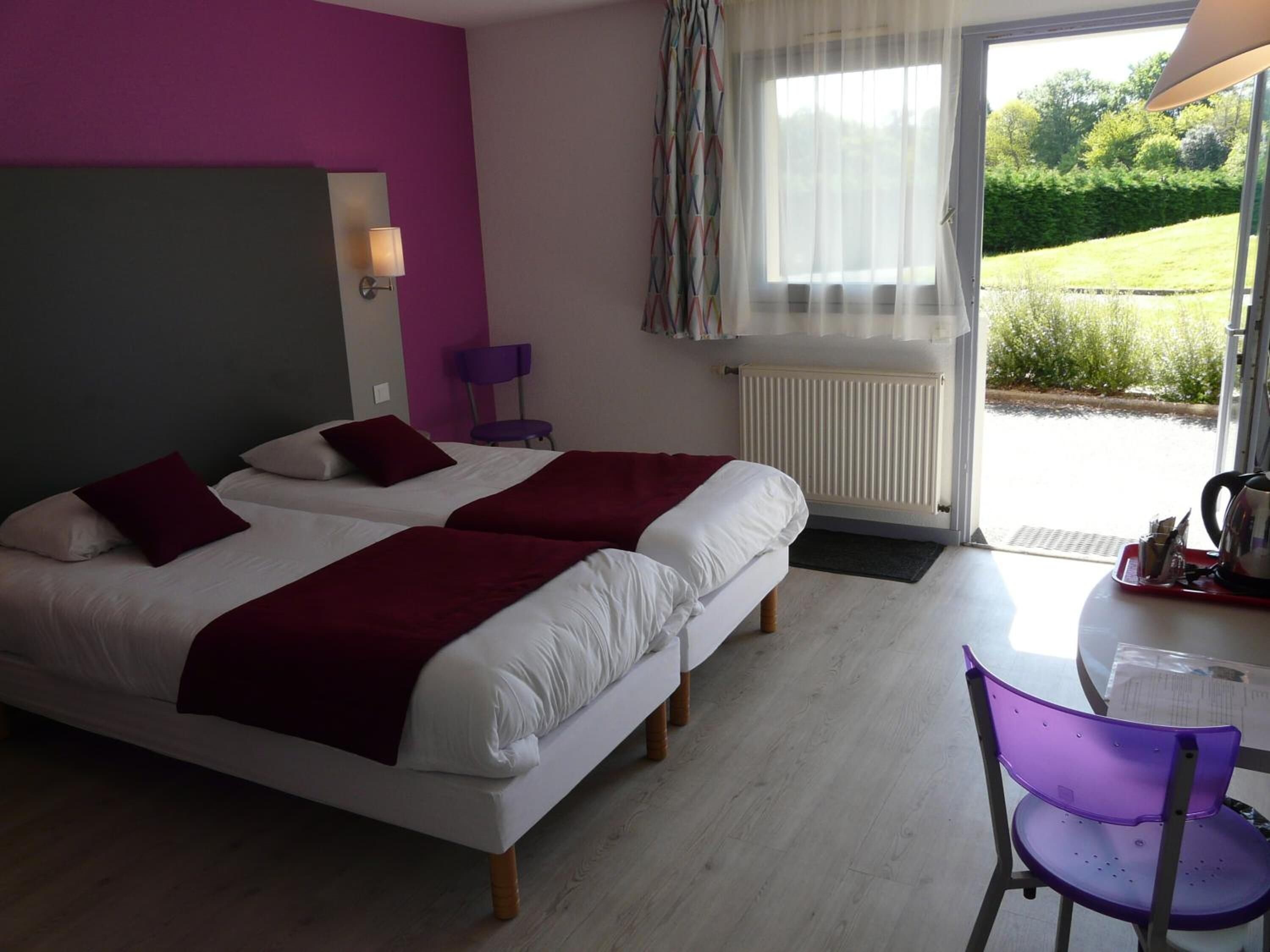 Una habitación de hotel con dos camas, una silla, una mesa y vistas al exterior.