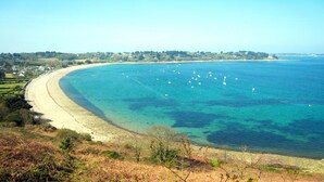 Un paisaje costero con una playa arenosa, aguas azules cristalinas y una costa distante con edificios.