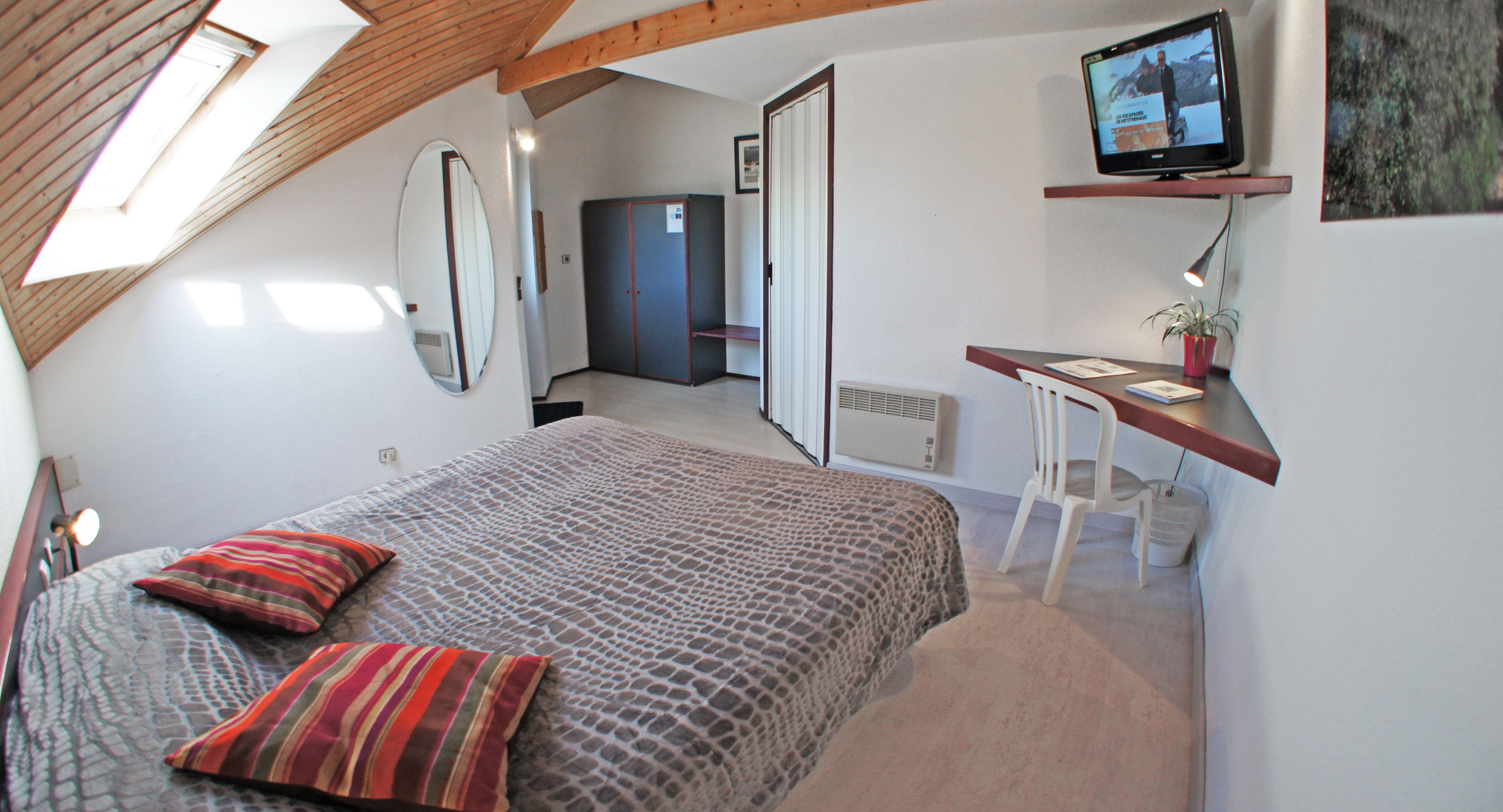 Un dormitorio con cama, escritorio, silla, televisor y armario.