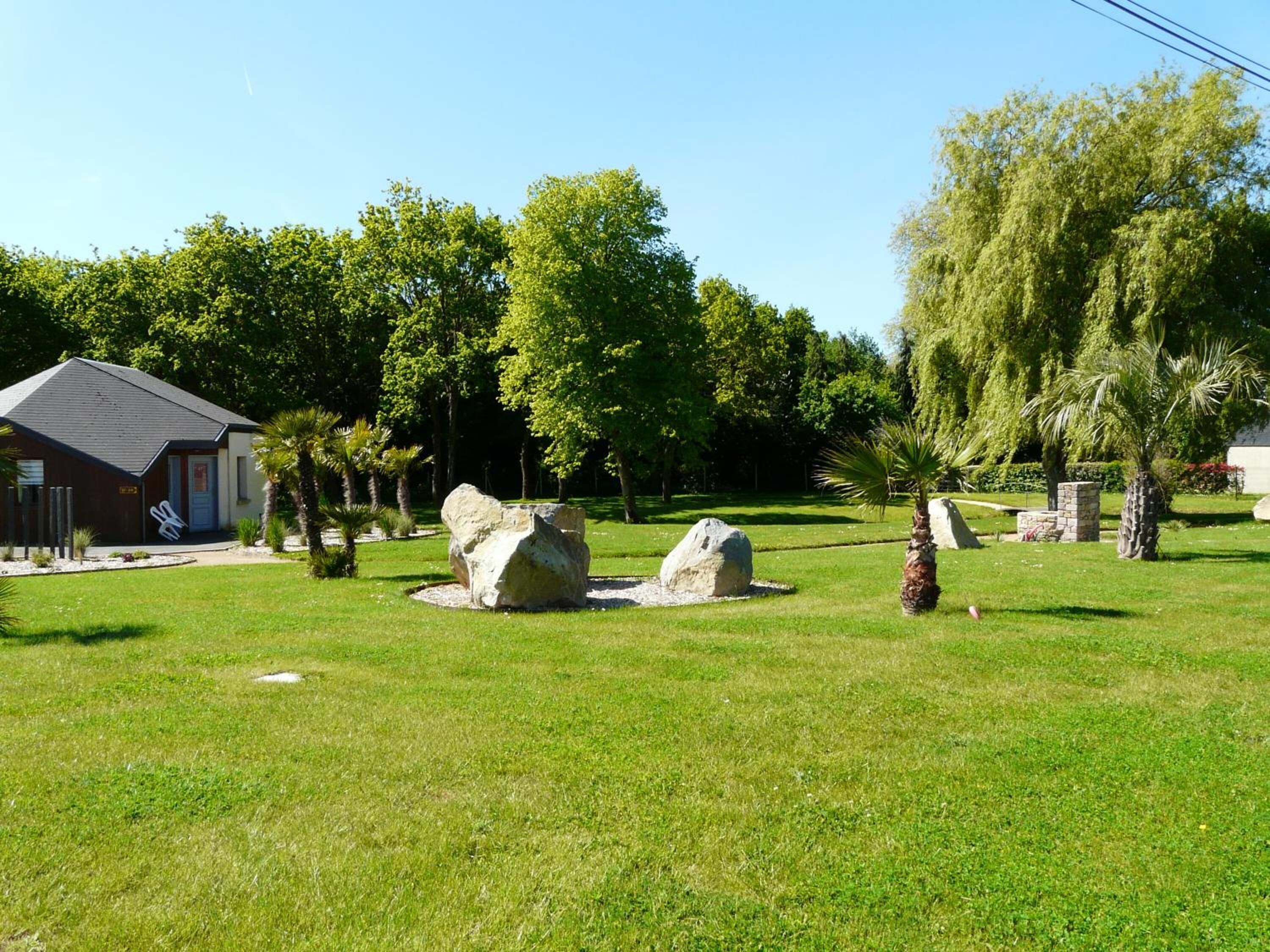 A grassy area with two large rocks, a small building, and trees.