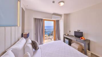 A hotel room with a bed, a desk with a TV, and a balcony with a view of the sea.