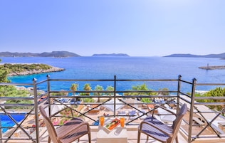 Un balcón con vista al mar, sillones de descanso, una mesa con una bandeja de frutas y bebidas, y una piscina al fondo.