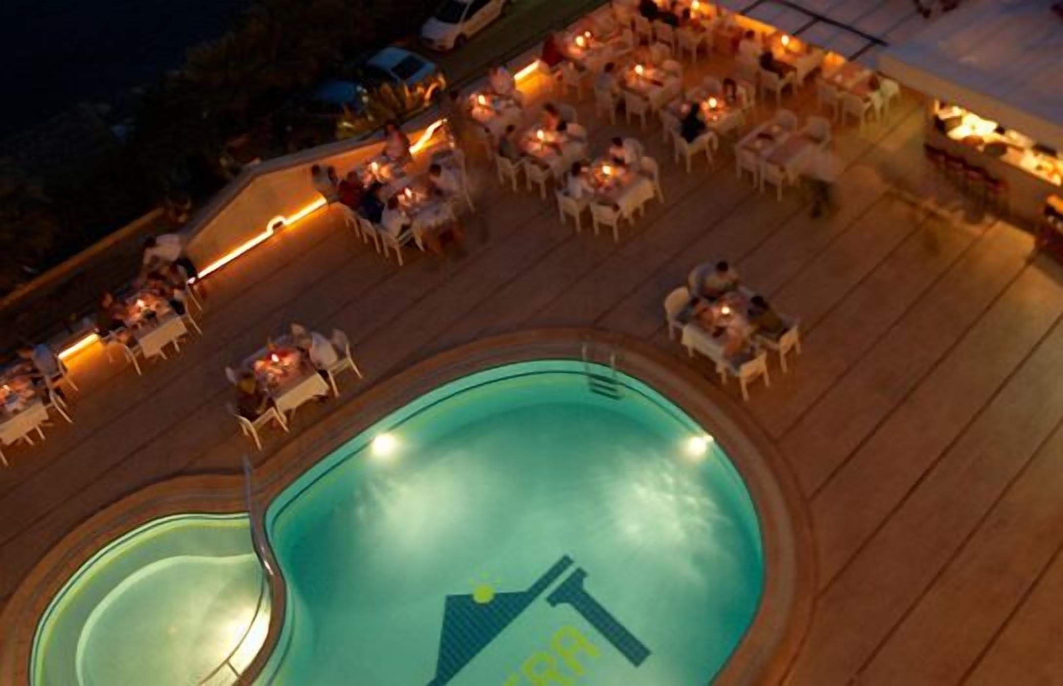 An outdoor pool area with multiple dining tables and chairs, surrounded by a wooden deck.