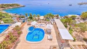 A pool area with a view of the sea, lounge chairs, umbrellas, and a small boat in the distance. - Hera Hotel Kas (Kaş)