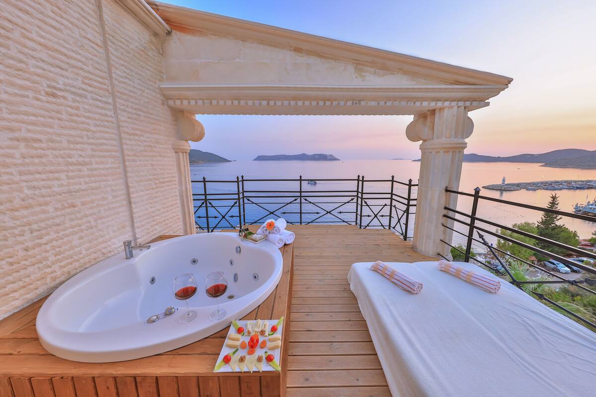 Un balcón con un jacuzzi, una terraza de madera y vista al mar.