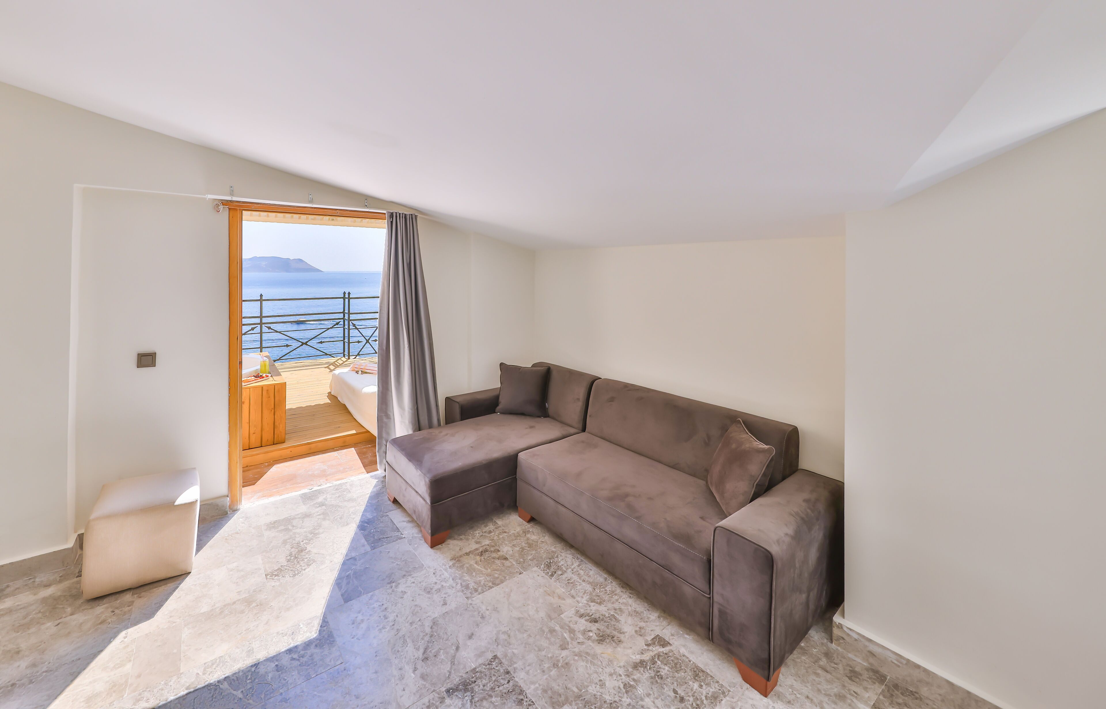 Ein modernes Wohnzimmer mit einem großen braunen Ecksofa, einem Holztisch und Meerblick durch eine Glastür.