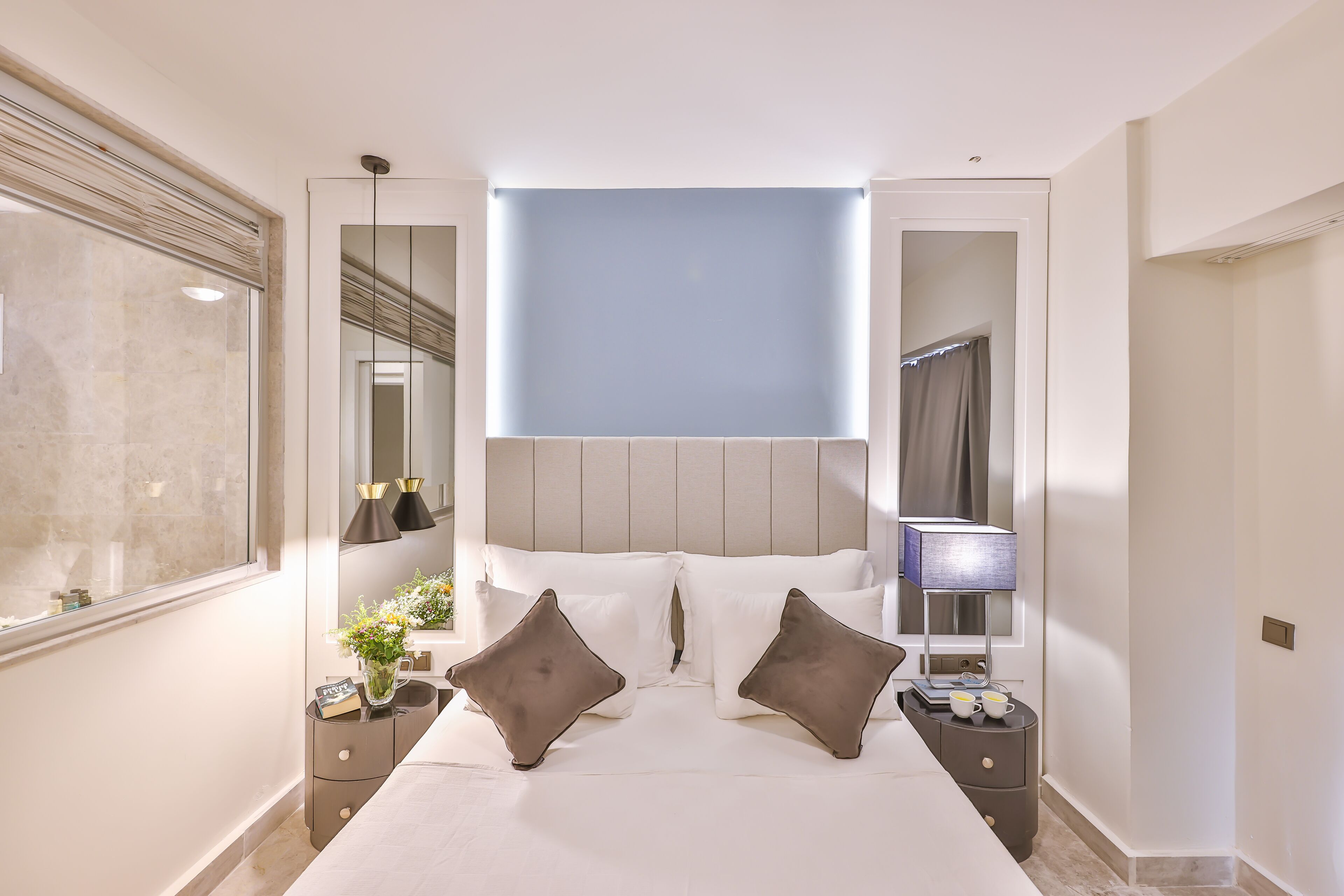 Une chambre à coucher moderne avec un grand lit, des tables de chevet, une commode, un miroir et une fenêtre.