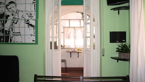 Une pièce avec un mur vert, une œuvre d’art en noir et blanc, un téléviseur et une fenêtre donnant sur l’extérieur.