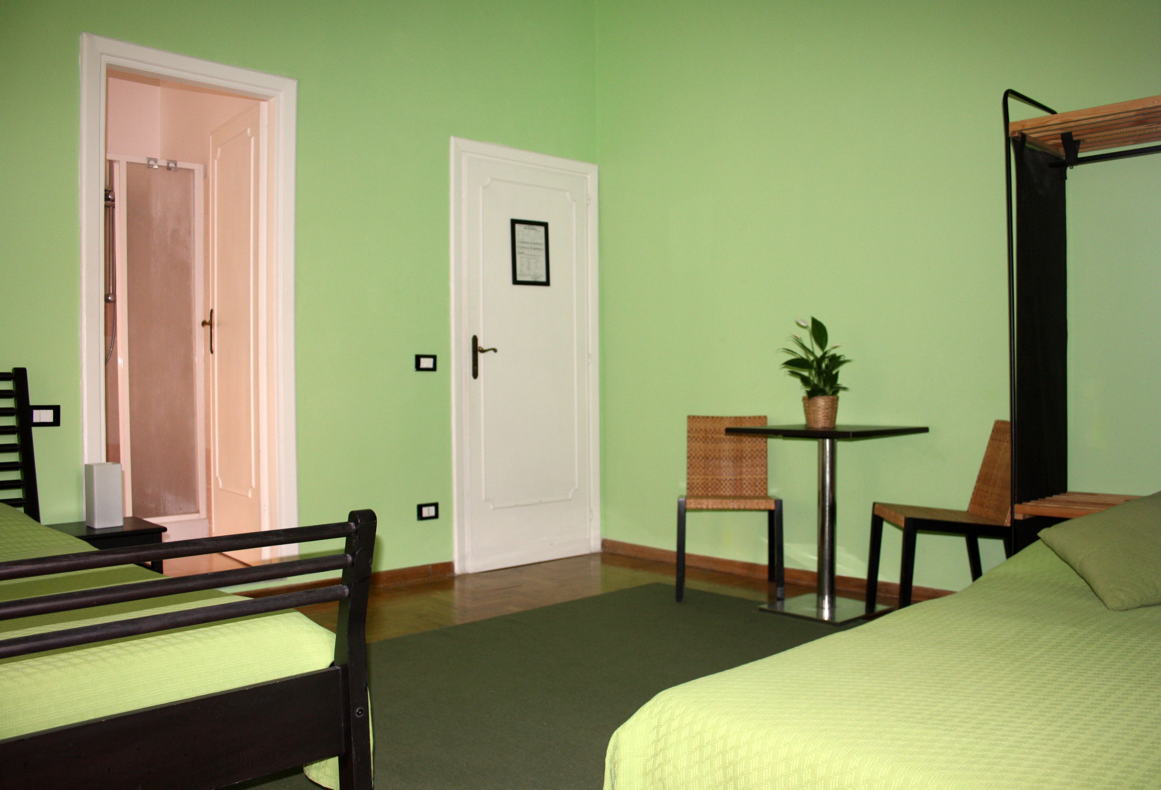 A room with two beds, a chair, a table with a plant, and a door.