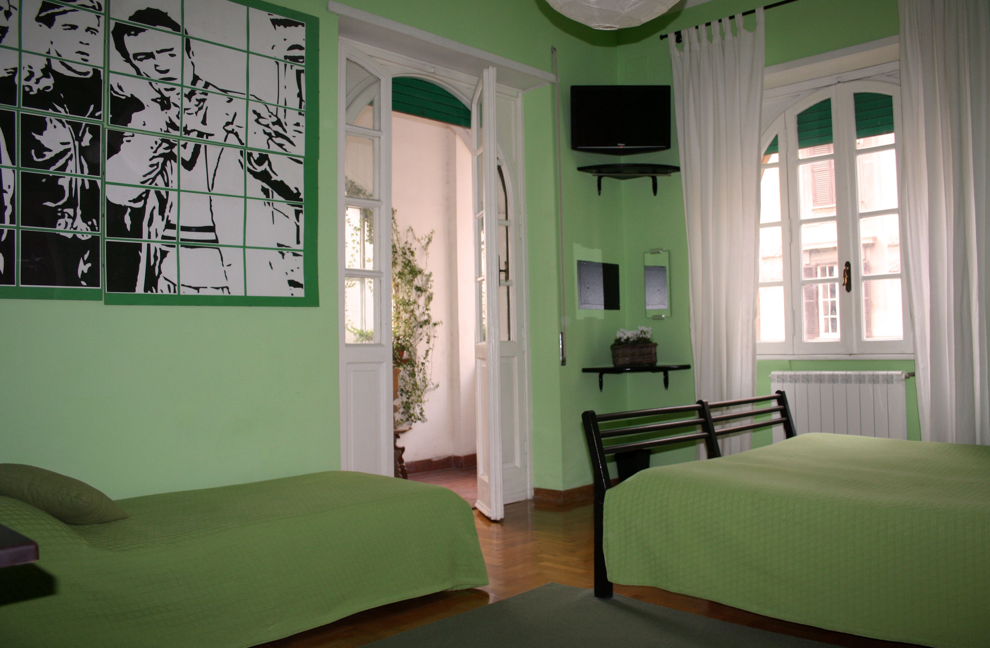 A room with two beds, a television, a plant, and a window with curtains.
