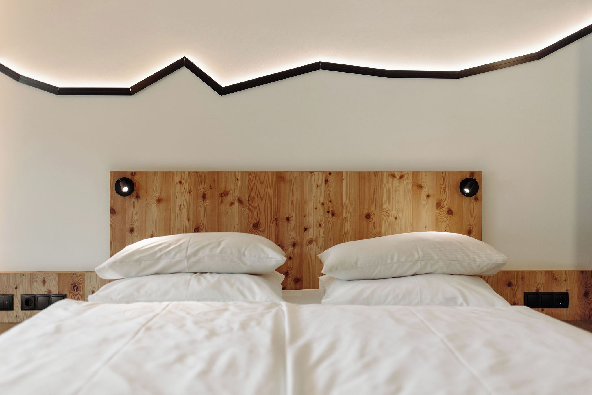 A double bed with white bedding, a wooden headboard, and wall-mounted reading lights.