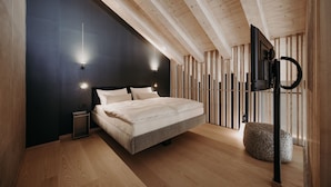 A modern bedroom with a large bed, wooden beams, a black accent wall, and a small bedside table. - Dips&Drops – SUPERIOR HOTEL · SPORTS · SPA · RESTAURANTS (Flachau)