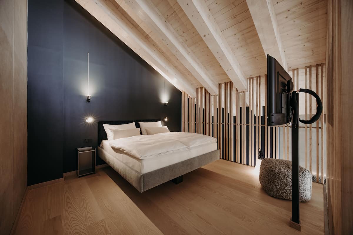 A modern bedroom with a large bed, wooden beams, a black accent wall, and a small bedside table.