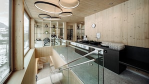 A modern interior with wooden walls, a glass staircase, and a kitchen area. - Dips&Drops – SUPERIOR HOTEL · SPORTS · SPA · RESTAURANTS (Flachau)