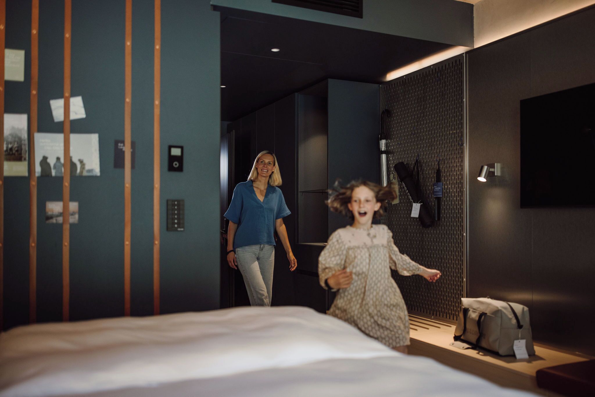 A modern hotel room with a bed, a bedside table, a lamp, and a wall with vertical stripes and pictures.