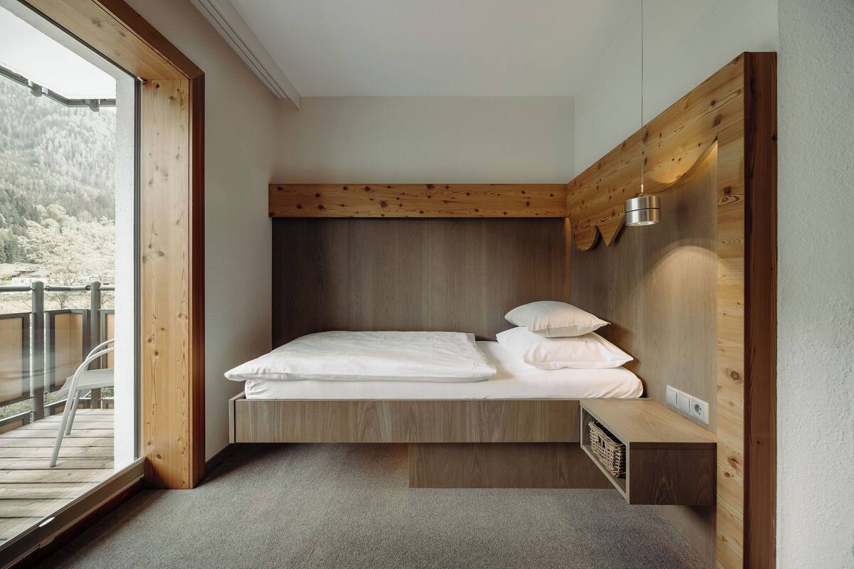 A bedroom with a built-in bed, a wooden headboard, a bedside table, and a view of a balcony.