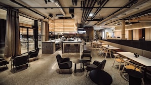 A modern restaurant with a bar area, seating arrangements, and a visible kitchen in the background. - Dips&Drops – SUPERIOR HOTEL · SPORTS · SPA · RESTAURANTS (Flachau)