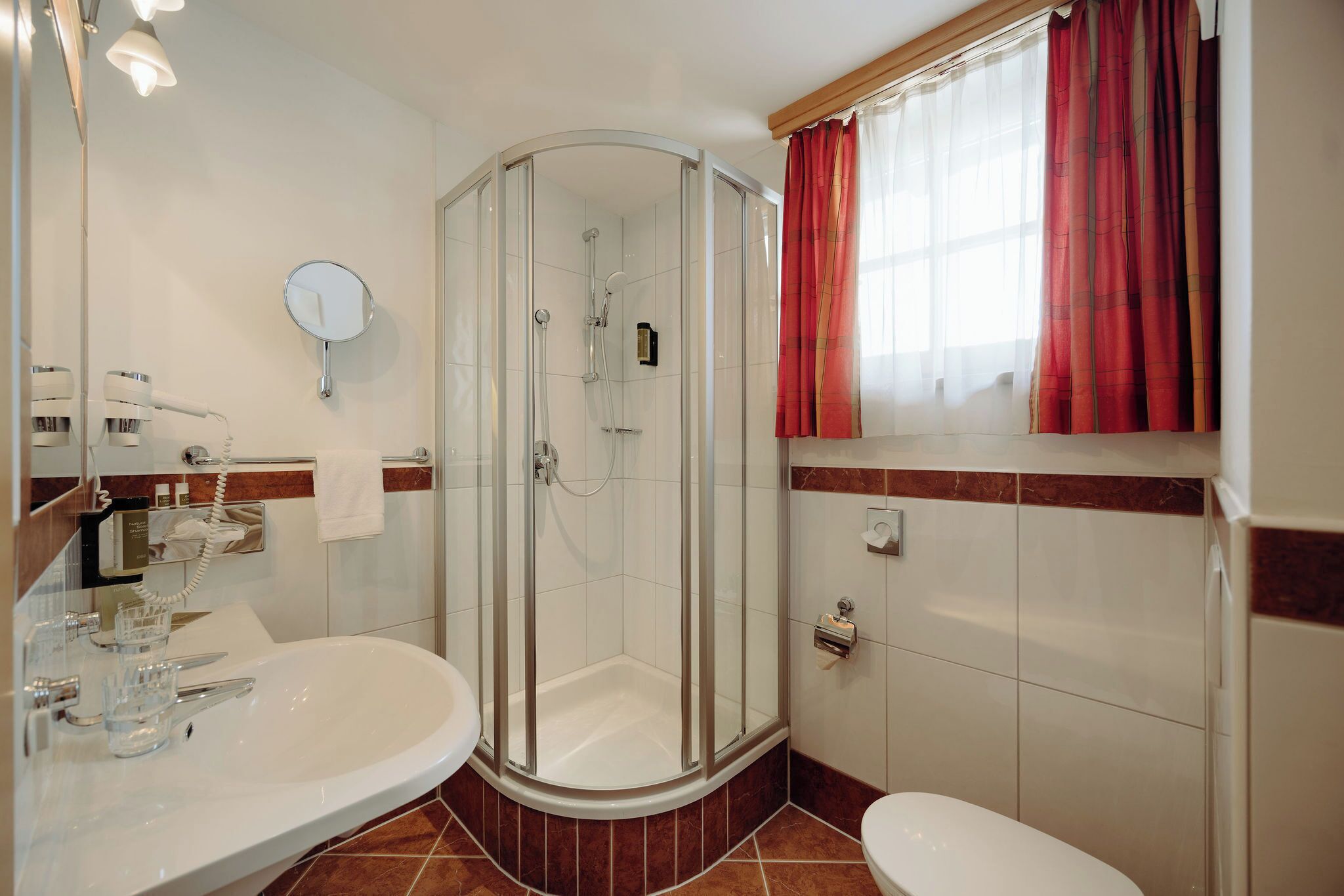 A bathroom with a glass-enclosed shower, a sink, a toilet, and a mirror.