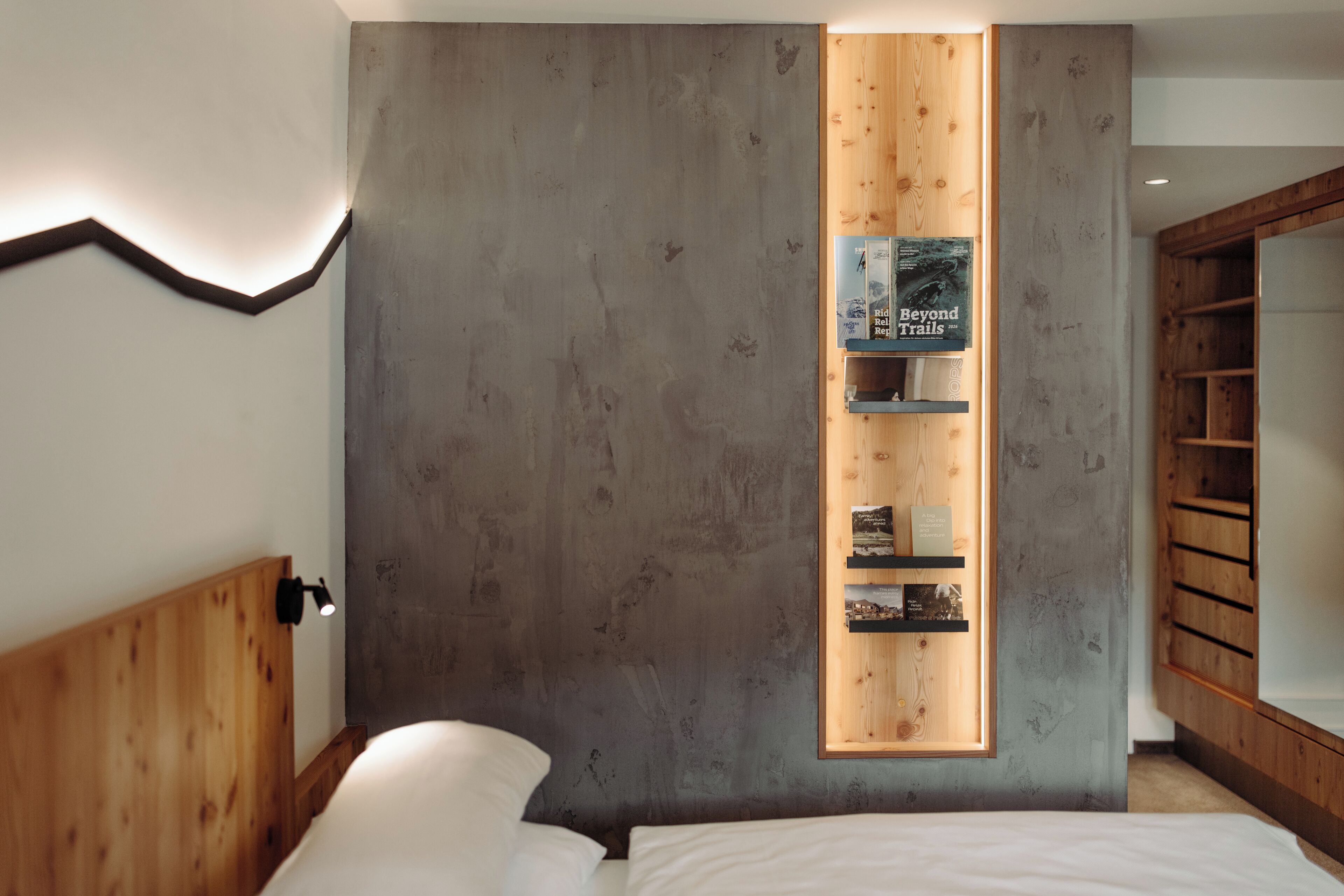 Un dormitorio moderno con cabecera de madera, estantería empotrada con libros y un espejo grande.