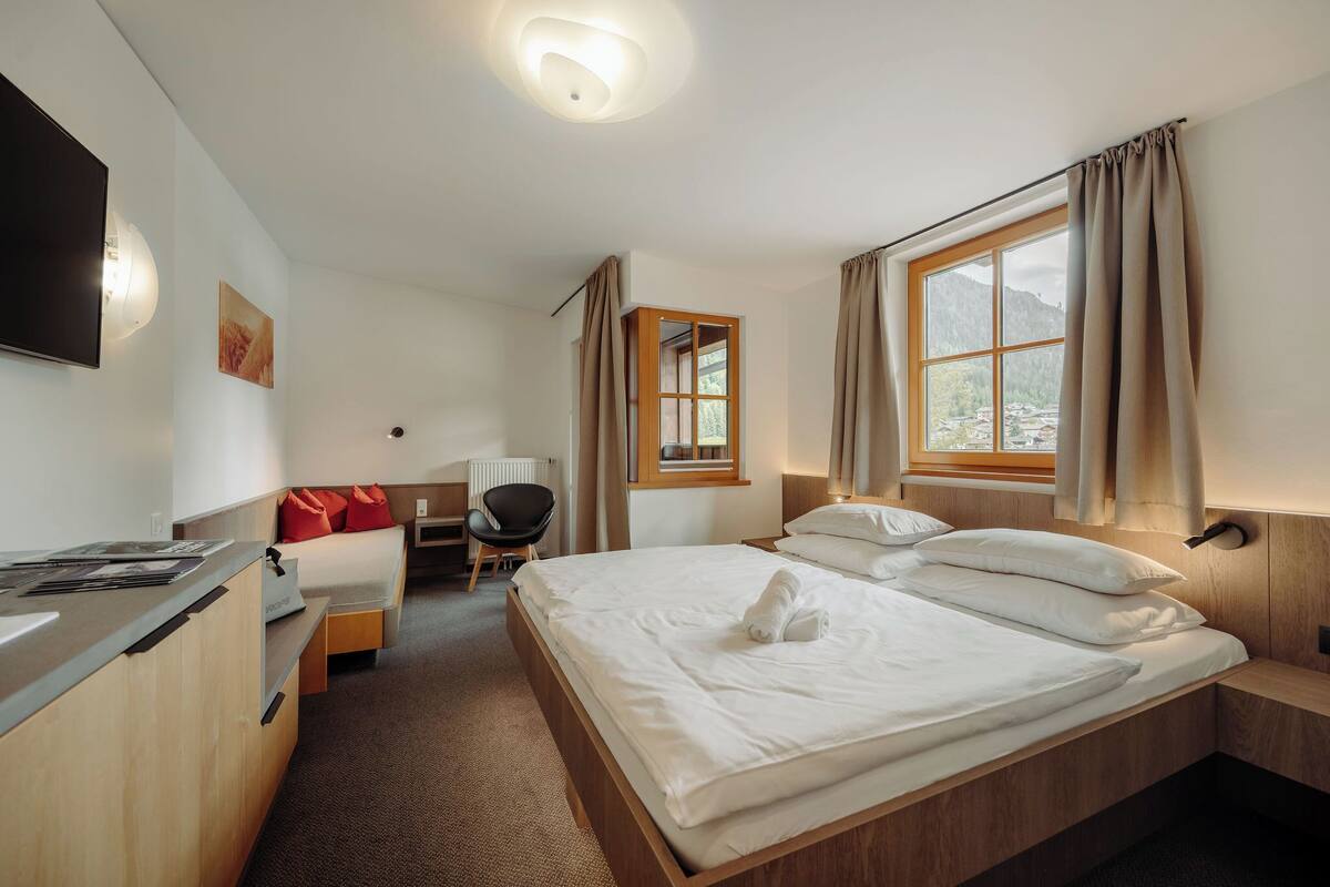 A hotel room with a bed, a desk, a chair, a TV, and a window with curtains.