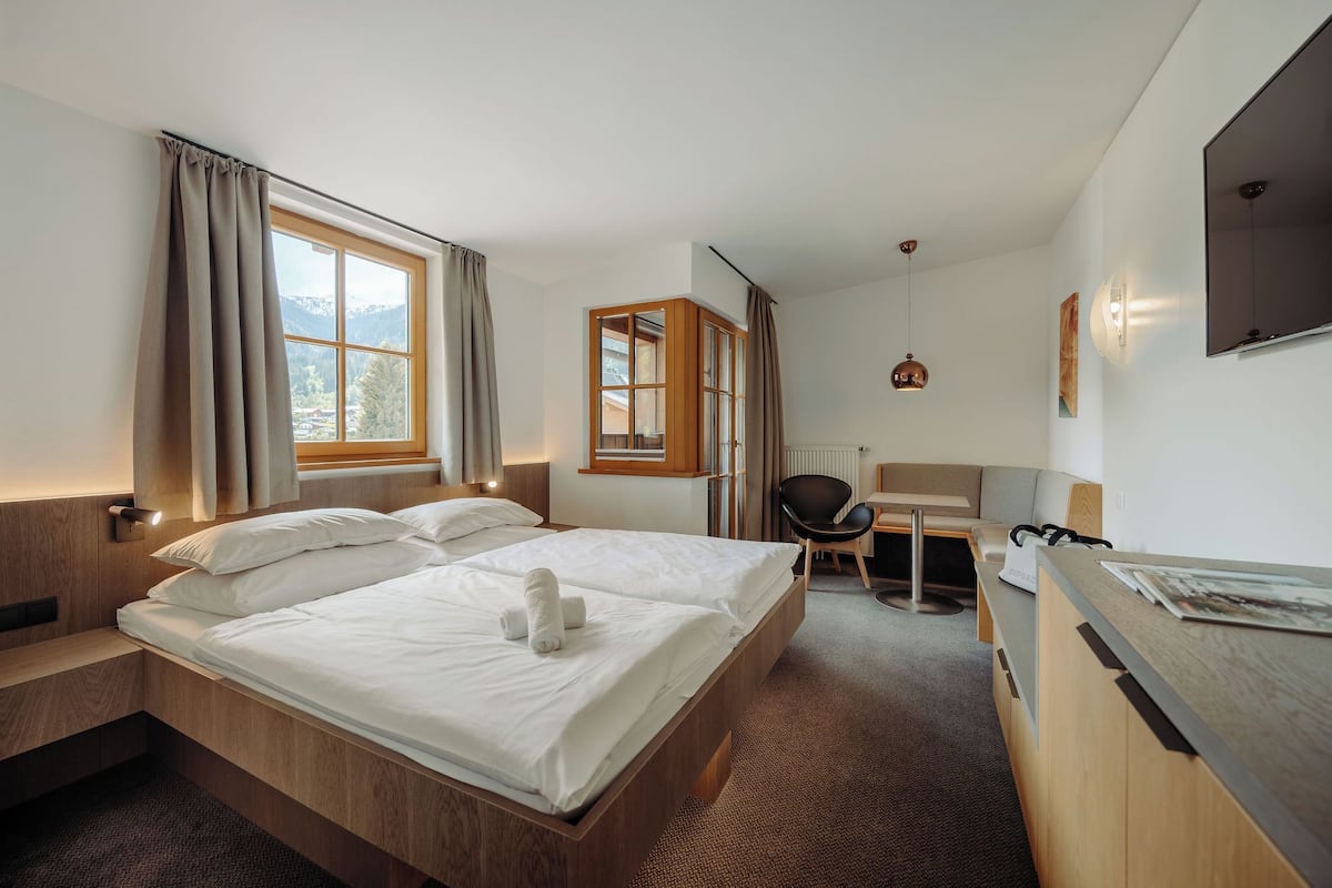 A hotel room with a bed, desk, chair, and a view of mountains through the window.
