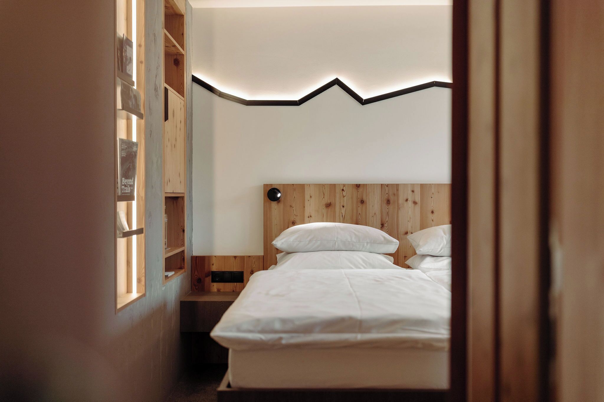 Un dormitorio con cabecera de madera, una cama con ropa de cama blanca y una mesita de noche.