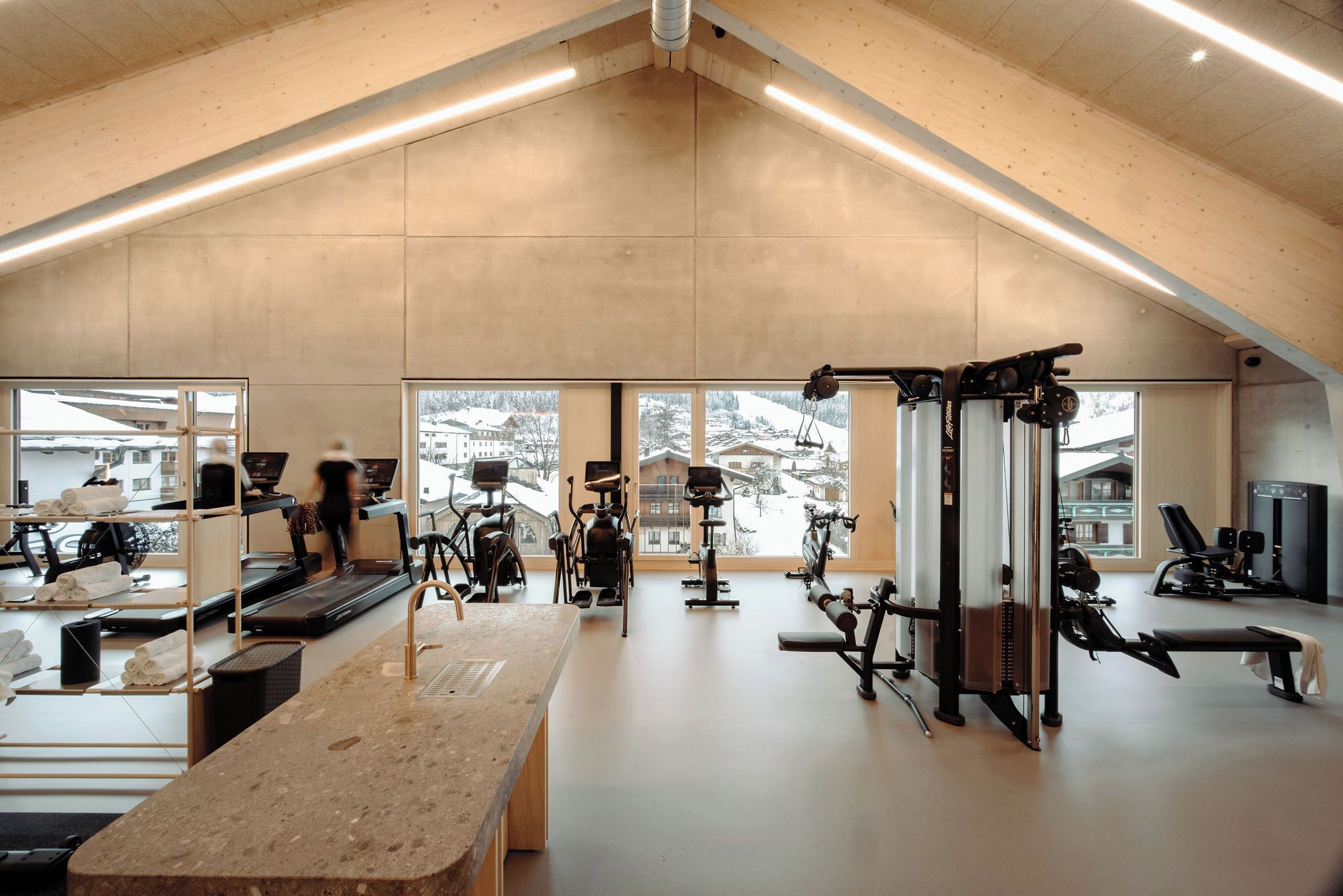 A spacious gym with various exercise equipment, large windows, and a high ceiling.