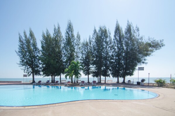 Una piscina con sillones de descanso y árboles, cielo despejado y vista al mar.