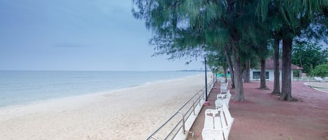 A beach with white chairs and a railing along the shore.