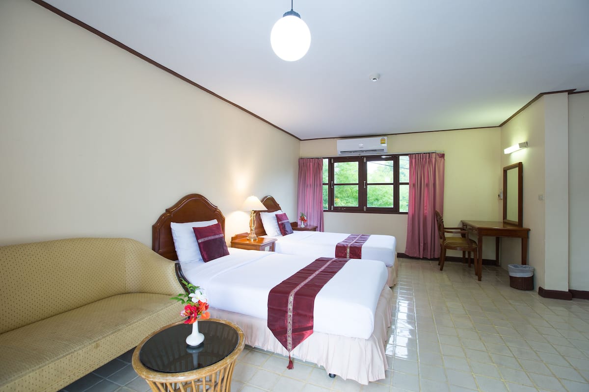 Une chambre d’hôtel avec deux lits, un canapé, une petite table avec un vase, un bureau et une chaise.