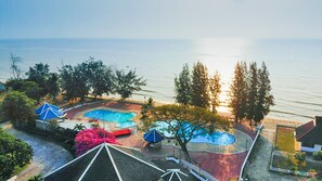 Una propiedad costera con piscina, sombrillas y vistas al mar.