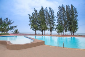 A swimming pool with a curved edge, surrounded by trees and a view of the sea. - Eurasia Cha-Am Lagoon (Cha-am)