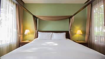 A large bed with two bedside lamps, a wooden headboard, and sheer curtains.