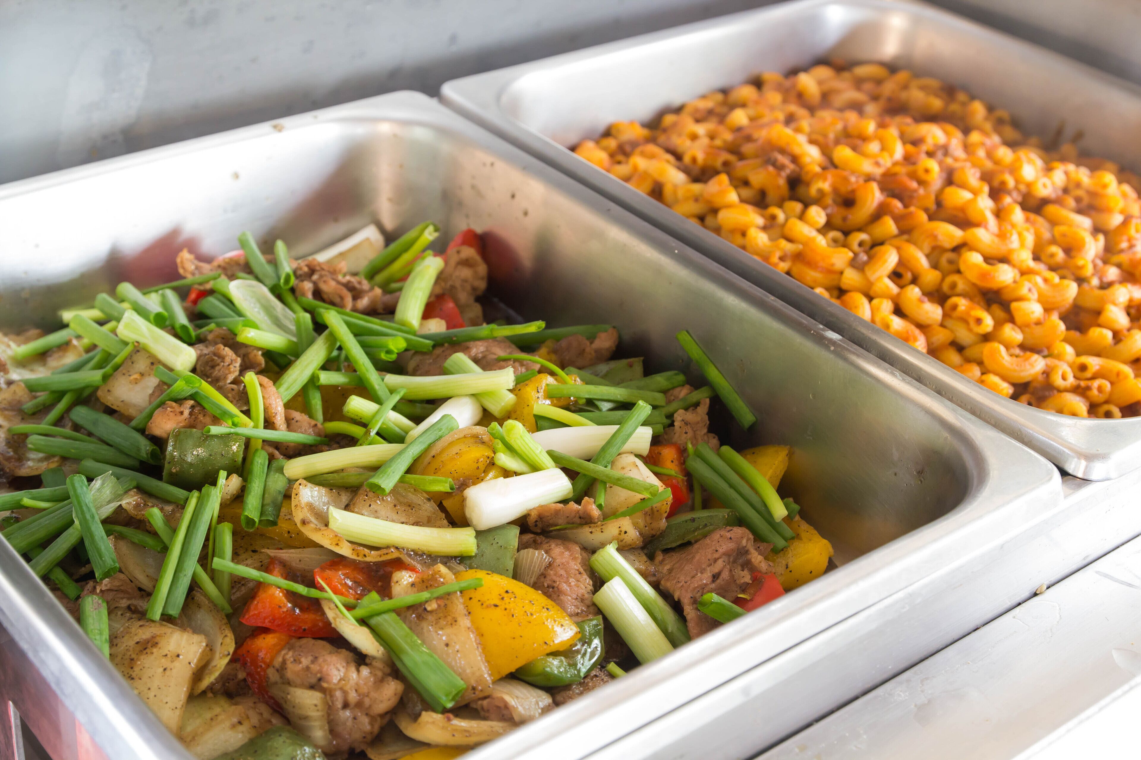 Un buffet proposant divers plats, notamment des viandes et des légumes sautés, ainsi que des macaronis au fromage.
