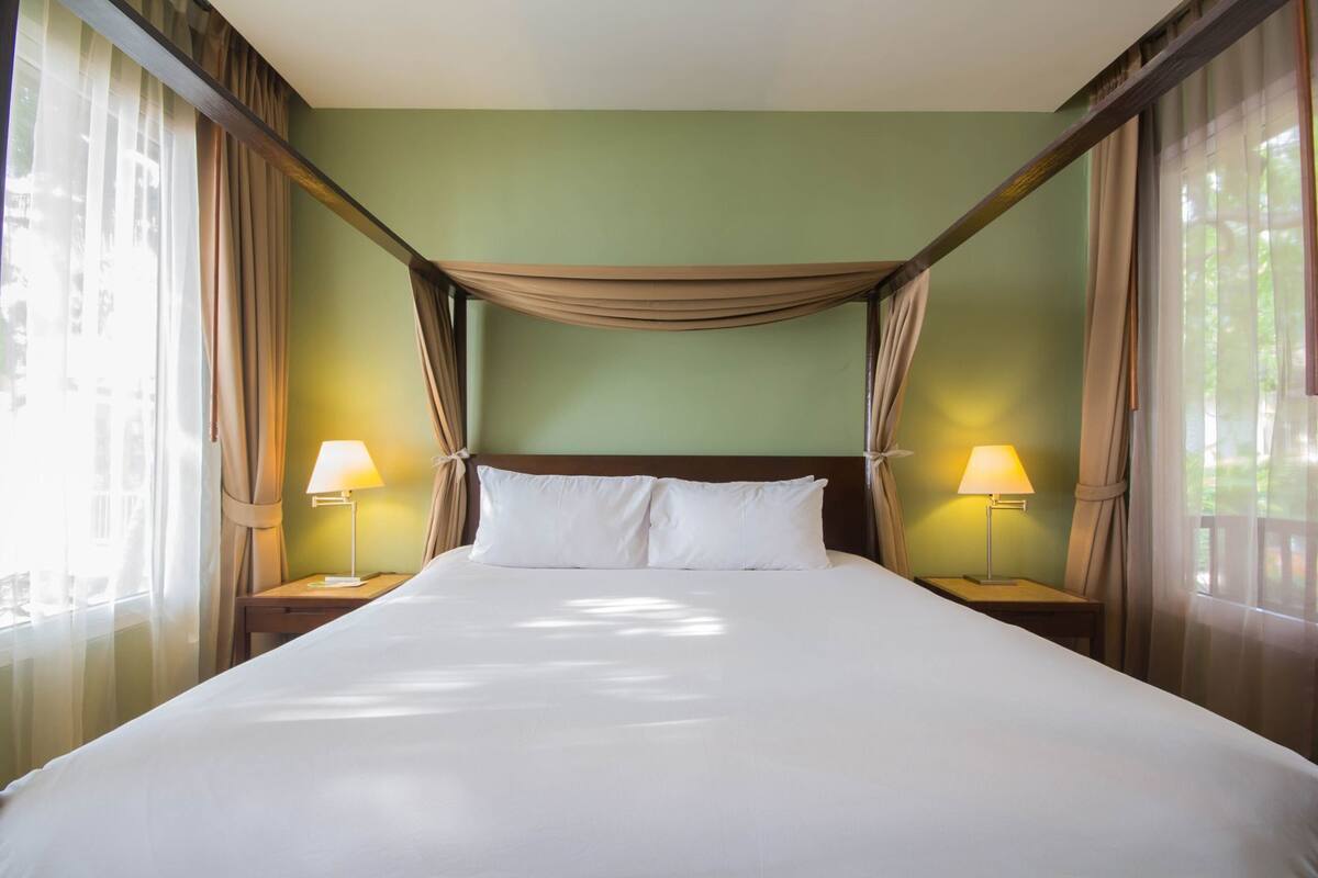 Een hotelkamer met een groot bed, twee bedlampen en dunne gordijnen.