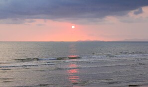 Un coucher de soleil sur une mer calme, où les vagues viennent doucement lécher le rivage.