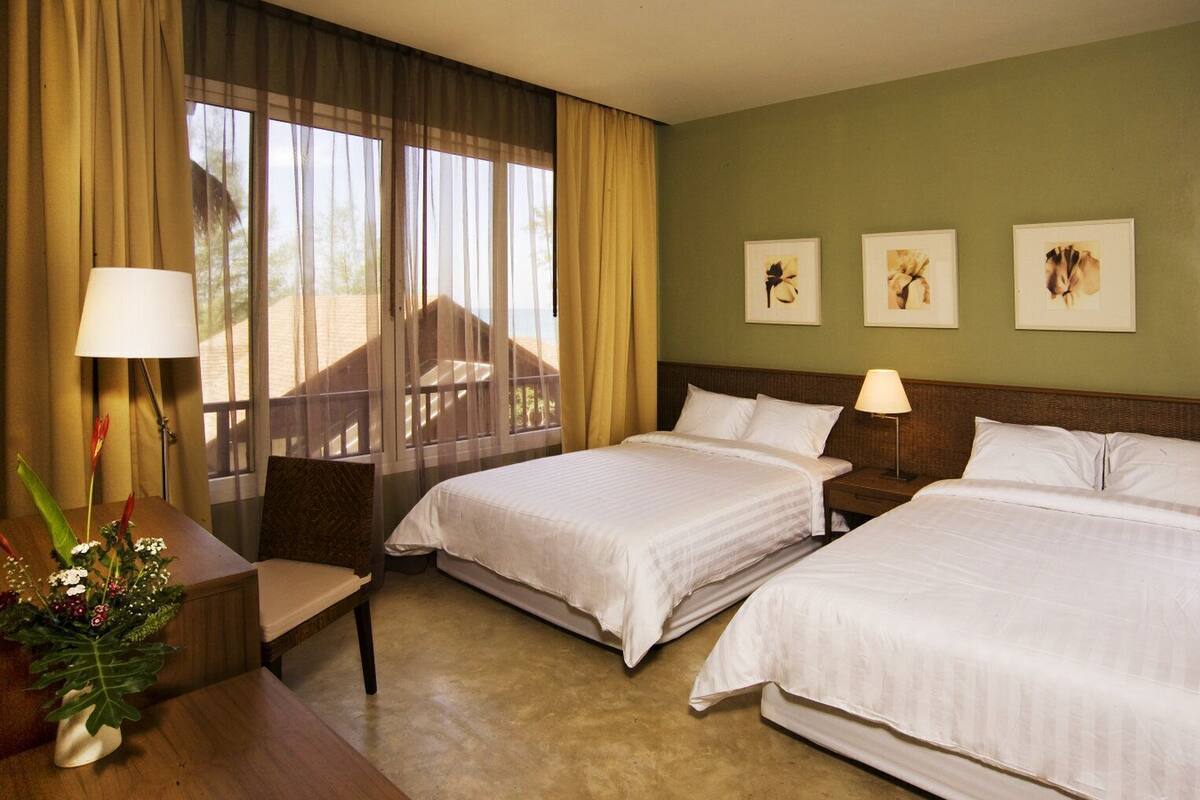 Een hotelkamer met twee bedden, een bureau, een stoel, een lamp en een raam met gordijnen.