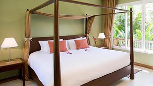 A four-poster bed with white linens and pink pillows, a nightstand with a lamp, and a view of greenery through large windows. - Centara Chaan Talay Resort & Villas (Trat)