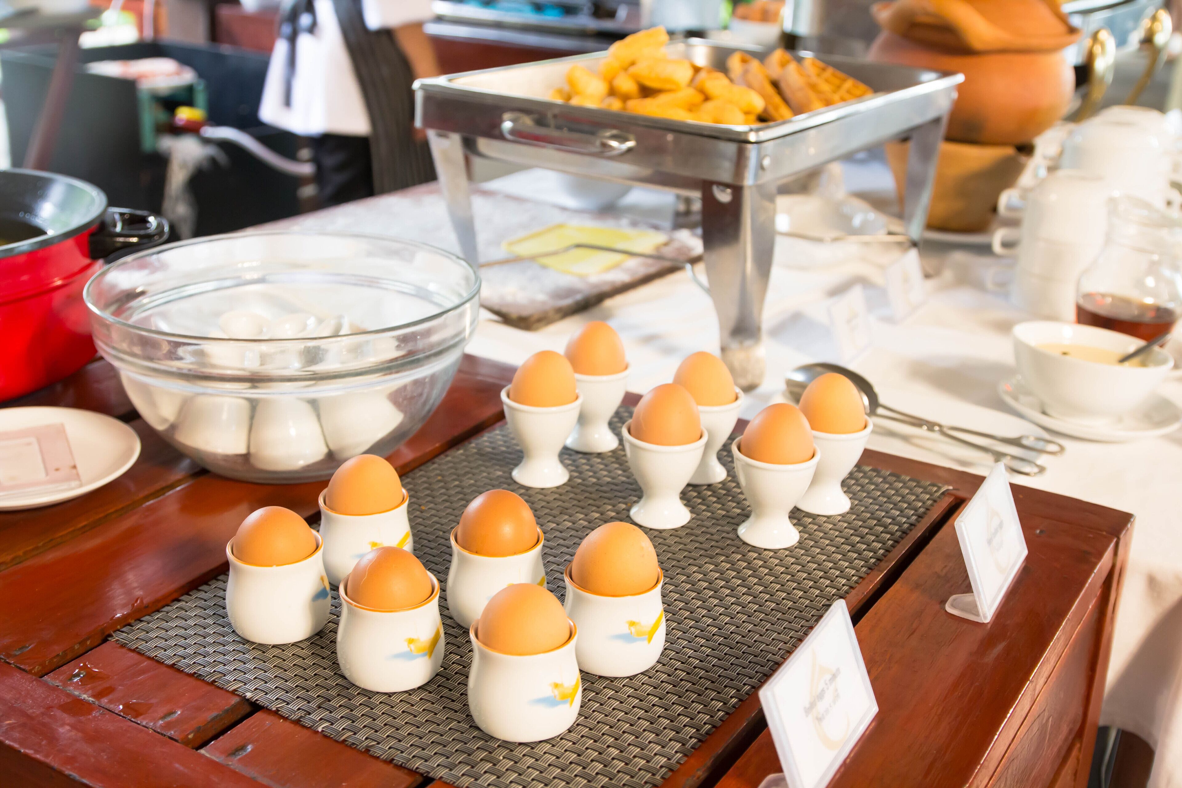 A breakfast buffet with various food items and a bowl of eggs arranged on a table.