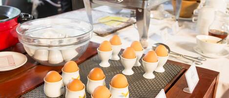 A breakfast buffet with various food items and a bowl of eggs arranged on a table.