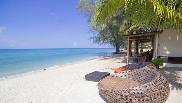 A beach with a wicker lounge chair, a small table, and a covered seating area with a palm tree. - Centara Chaan Talay Resort & Villas (Trat)