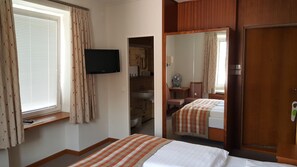 A hotel room with a bed, a television, a mirror, a window with curtains, a sink, and a door. - Hotel Hohenstauffen (Salzburg)
