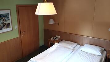 Una habitación de hotel con cama, mesitas de noche, lámpara, un cuadro en la pared y una puerta.