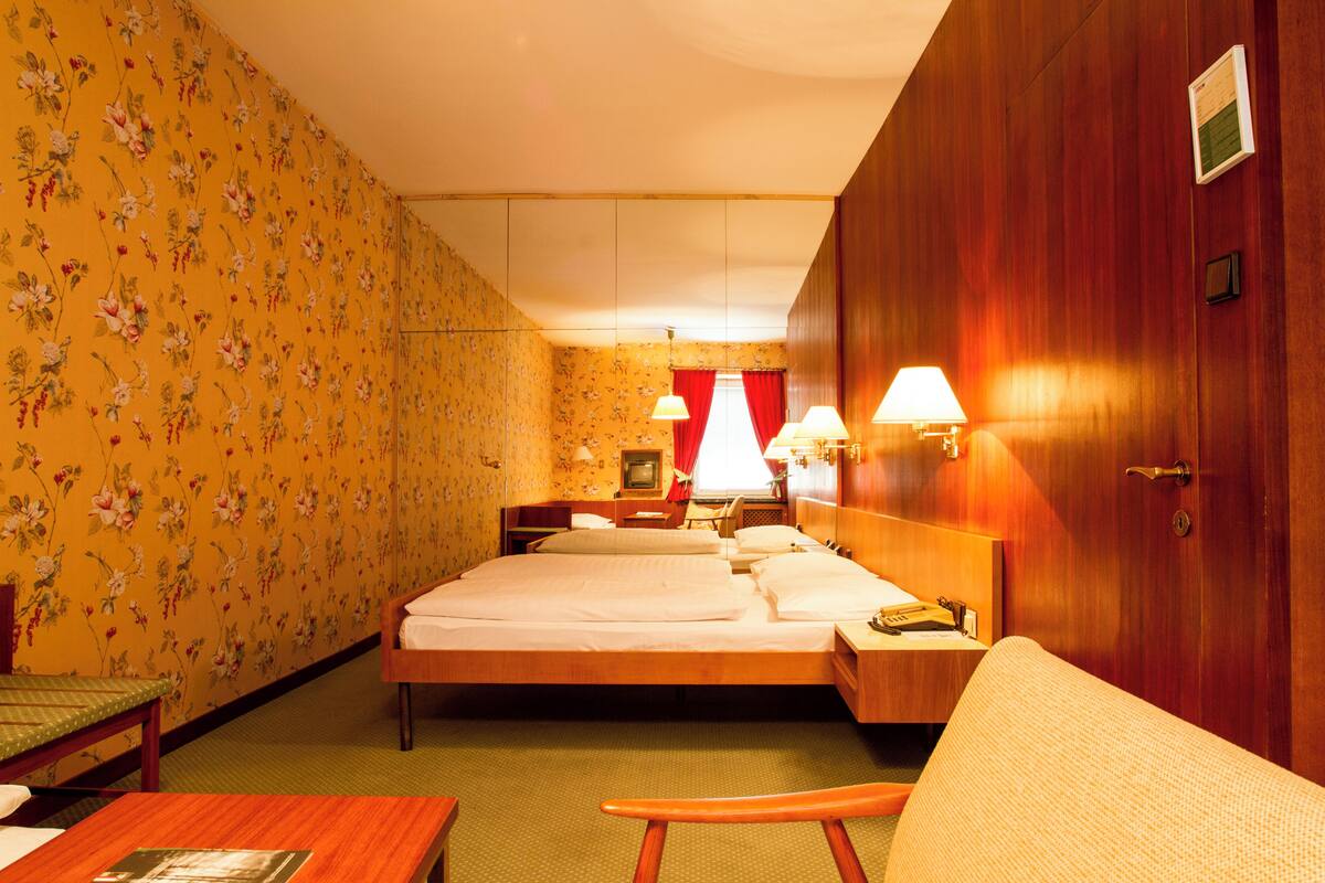 Une chambre d’hôtel avec un papier peint à motifs floraux, un lit, un bureau et une chaise.