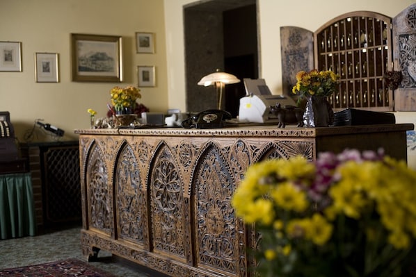A reception desk with intricate carvings, framed pictures on the wall, and a vase with flowers.