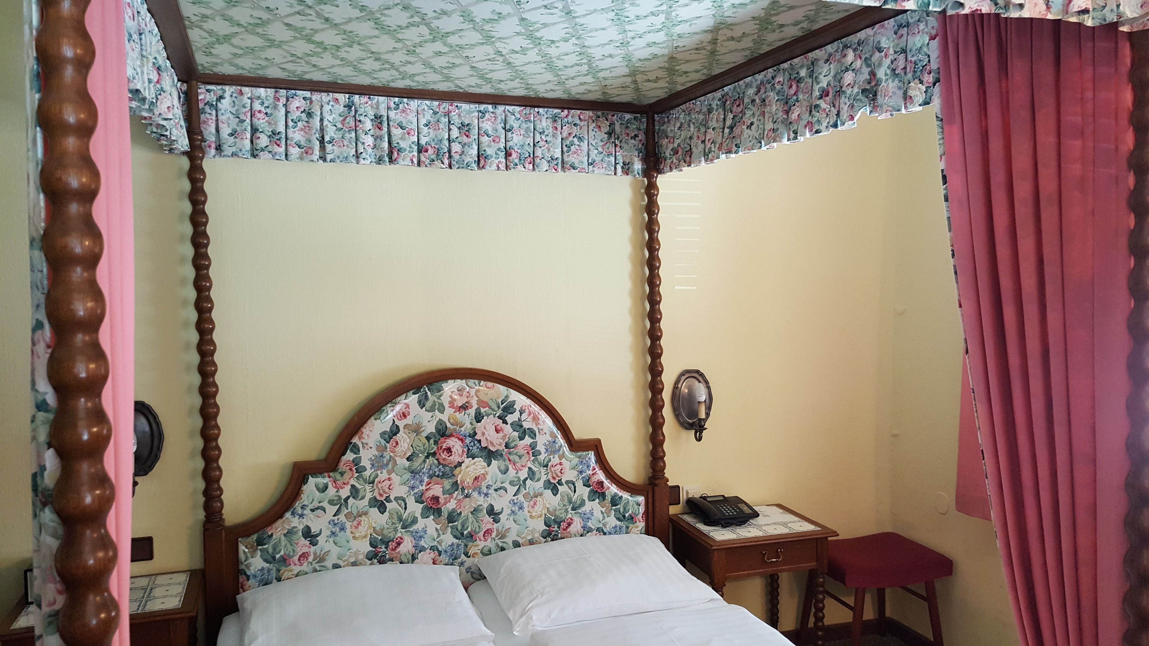 Una cama con dosel, un tablero de noche con teléfono y una cortina roja.