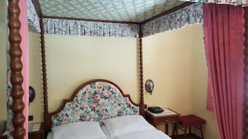 Una cama con dosel, un tablero de noche con teléfono y una cortina roja.