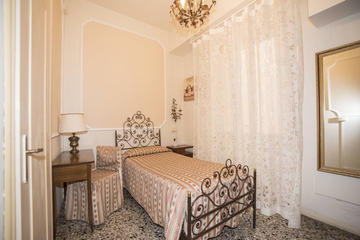 A bedroom with a bed, a bedside table, a lamp, a mirror, and a curtain.