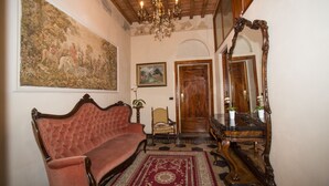 A traditional interior with a red upholstered sofa, a wooden chair, a large mirror, and a chandelier. - Relais Centro Storico Pisa (Pisa)
